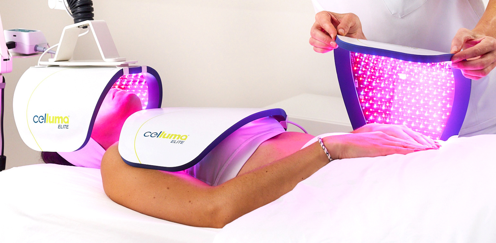 Woman laying on a bed in a health spa receiving red LED light therapy from 3 Celluma devices positioned on her head and torso